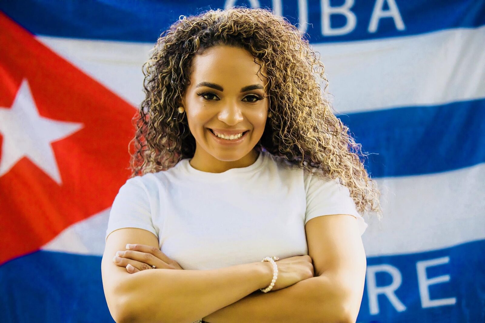 Ereka Howard smiling with arms crossed in front of the Cuban flag